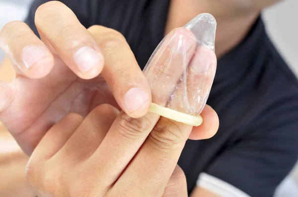 Jovem desenrolando um preservativo em seus dedos — Fotografia de Stock