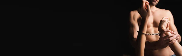 Ausgeschnittene Ansicht eines hemdlosen Mannes mit Handschellen auf Freundin isoliert auf schwarz, Banner — Stockfoto
