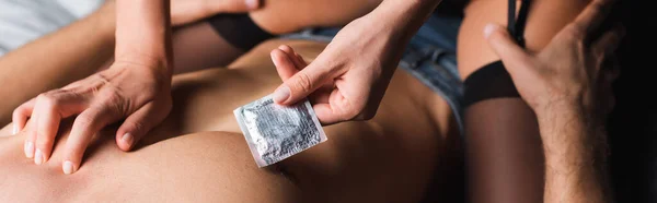 Обрізаний вид жінки в панчохах тримає презерватив біля без сорочки на ліжку, банер — стокове фото