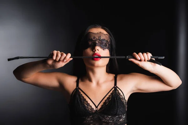 Sexy woman in lace bra and mask holding spanking paddle on black background — Stock Photo