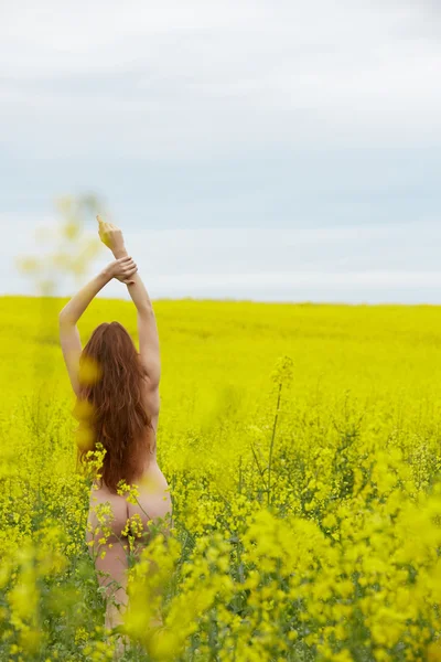 Рапсовое поле с жёлтыми цветами, обнаженная рыжеволосая девушка стоящая — стоковое фото