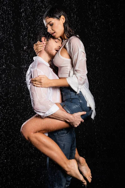 Sexy romántico pareja en mojado blanco camisas abrazo y besos en gotas de lluvia en negro fondo - foto de stock