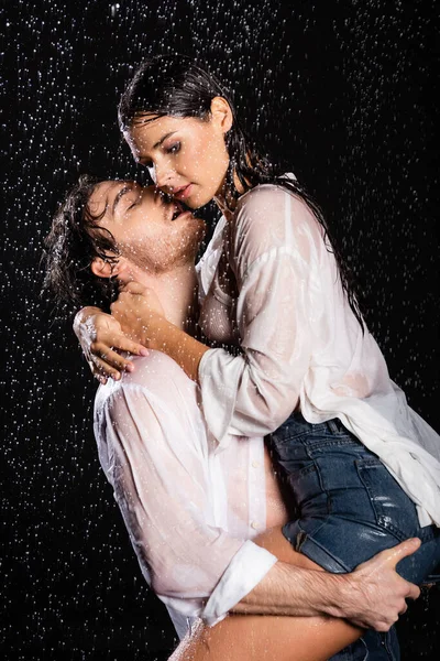 Sexy romantic couple in wet white shirts passionately hugging in rain drops on black background — Stock Photo