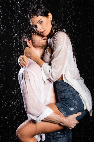 Сексуальная романтическая пара в мокрой одежде страстно обнимающая капли дождя на черном фоне — стоковое фото