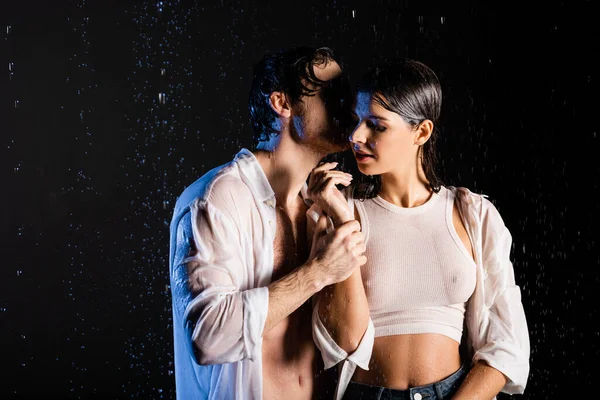 Bagnato coppia appassionata che si tiene per mano e abbraccia in gocce di pioggia su sfondo nero — Foto stock