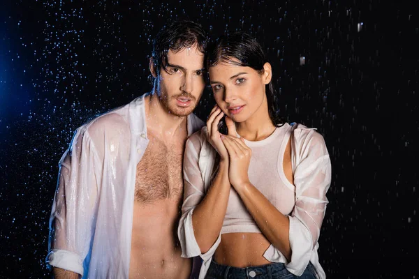 Passionate sexy couple in wet clothes standing in rain drops on black background — Stock Photo