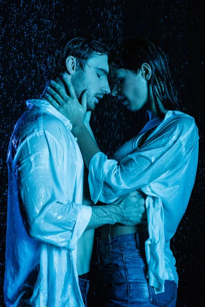 Passionate romantic couple gently hugging in water drops on black background with blue color filter — Stock Photo