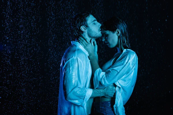 Wet passionate romantic couple gently hugging in water drops on black background with blue color filter — Stock Photo