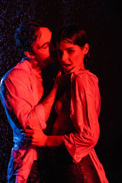 Rouge et bleu couleurs filtres image de femme séduisante sexy humide et homme passionné étreignant dans des gouttes d'eau sur fond noir — Photo de stock