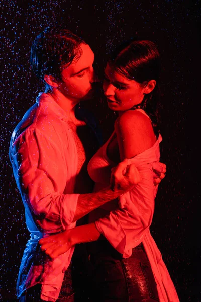 Cores vermelhas e azuis filtros imagem de casal romântico sexy molhado apaixonadamente abraçando gotas de água no fundo preto — Fotografia de Stock